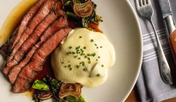 Close-up of Bûcheron’s signature steak dish with mashed potatoes, caramelized shallots, and seasonal greens.