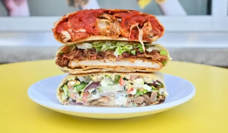 A plate stacked with three grilled hexagon-shaped tortilla pockets, each filled with different colorful ingredients like lettuce, beef, tomatoes, and creamy sauces, showcasing Hippo Pockets' creative take on the iconic Taco Bell Crunchwrap for a fast-casual audience.