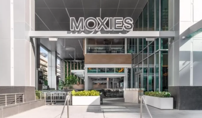 Street-level view of Moxies restaurant exterior in a modern urban setting, showcasing the upscale-casual design style central to its U.S. expansion strategy.
