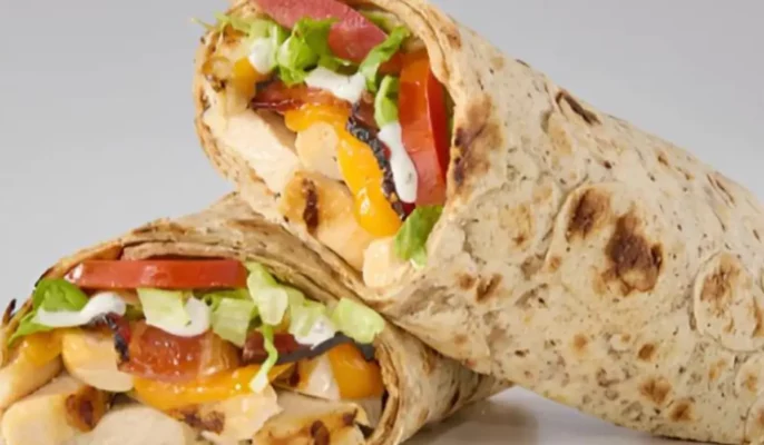Close-up of Potbelly’s new grilled chicken wrap with cheddar cheese, lettuce, tomatoes, and ranch dressing inside a multigrain flatbread wrap.