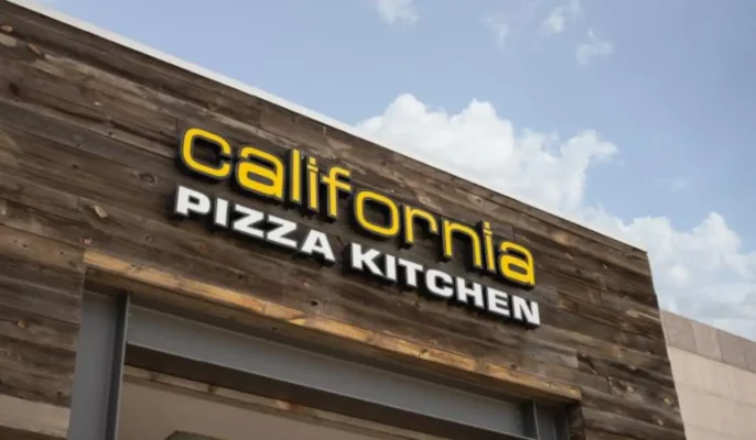 Close-up of the California Pizza Kitchen logo on the wooden exterior of a restaurant in Los Angeles, representing the brand’s identity amid ownership transition and acquisition news.