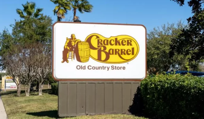 Cracker Barrel Old Country Store road sign featuring original logo with man and barrel, surrounded by palm trees and roadside foliage.