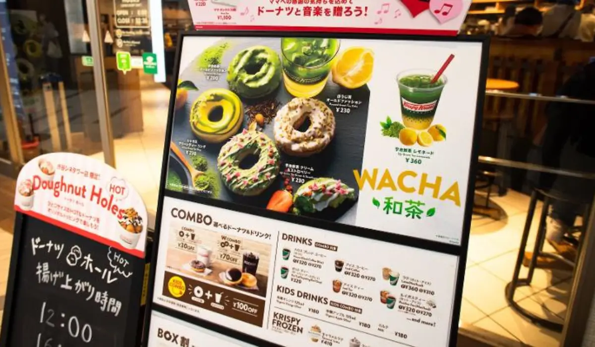 Matcha-themed Krispy Kreme doughnuts and beverages on a menu display in Japan, featuring combo pricing and specialty drink options at a store entrance.
