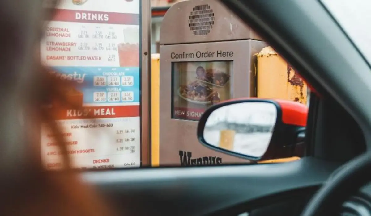 View from inside a vehicle at a fast-food drive-thru ordering station and menu board.